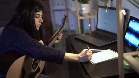 Musician-playing-guitar-in-room-and-taking-notes