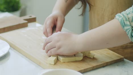 Woman-shifting-cheese-cubes-from-cutting-board-on-plate