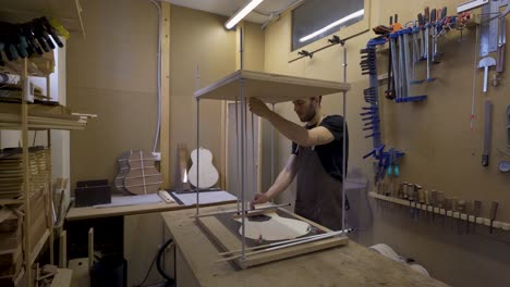 Craftsman-installing-metal-sticks-while-building-guitar-in-workroom