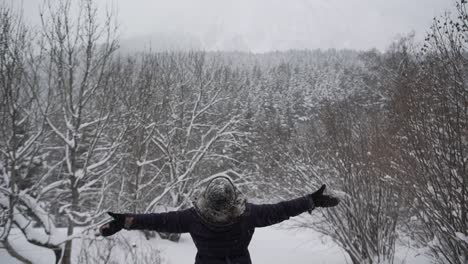 Anonymous-woman-in-outerwear-outstretching-arms-in-winter-forest