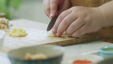 Woman-cutting-garlic-on-wooden-board-in-kitchen