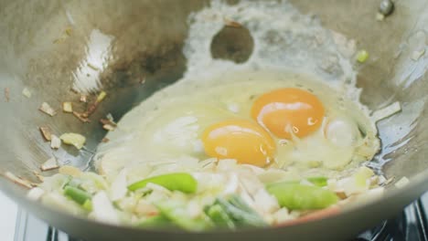 Person-mixing-eggs-in-pan-with-frying-vegetables