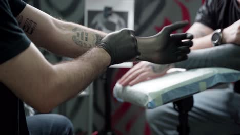 Unrecognizable-male-tattooist-putting-on-gloves-before-work-in-salon