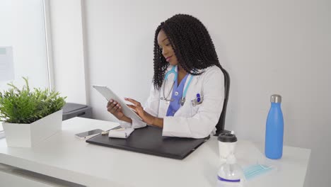 Smiling-black-woman-in-medical-uniform-using-tablet-in-hospital