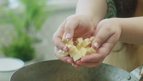 Woman-adding-cheese-cubes-in-frying-pan