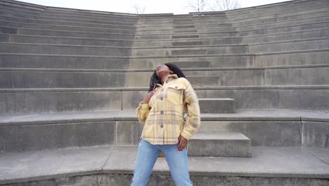 Smiling-black-woman-dancing-on-steps-in-park