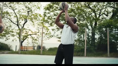 Eine-Schwarze-Person-In-Einem-Weißen-T-Shirt-Wirft-Effektvoll-Einen-Basketball-In-Den-Korb-Auf-Dem-Basketballplatz.-Video-In-High-Definition-Gefilmt