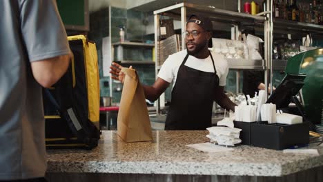 A-Black-person-in-glasses-gives-an-order-to-a-food-delivery-man-in-a-doner-market-and-shows-a-sign-of-approval.-Video-filmed-in-high-quality