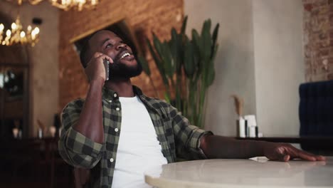 Black-person-laughing-while-talking-on-the-phone-in-a-cafe,-rest