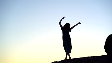 Female-silhouette-standing-gracefully-with-arms-raised-on-hilltop