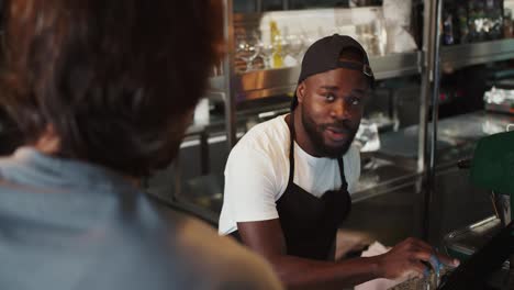 Doner-worker.-A-Black-person-in-a-black-cap-takes-an-order-on-an-electronic-guy-against-the-background-of-a-doner-market.-Service-in-a-fast-food-restaurant