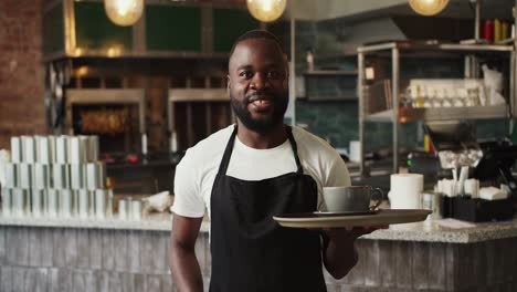 A-Black-person-in-an-apron-holds-a-tray-with-a-cup-of-coffee-and-poses-against-the-background-of-the-doner-market