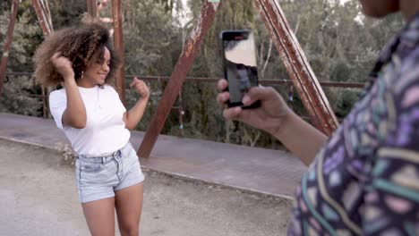 Schwarze-Frau-Filmt-Video-Eines-Fröhlichen-Freundes,-Der-Auf-Einer-Brücke-Tanzt