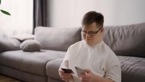 Young-man-with-down-syndrome-using-smartphone-and-credit-card-sitting-on-the-floor
