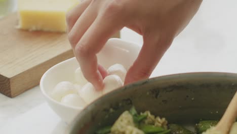 Crop-woman-adding-mozzarella-balls-to-pasta
