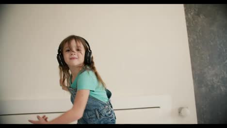 Fröhliches-Kleines-Mädchen-Tanzt,-Während-Es-Im-Wohnzimmer-Musik-Auf-Dem-Smartphone-Mit-Kopfhörern-Hört