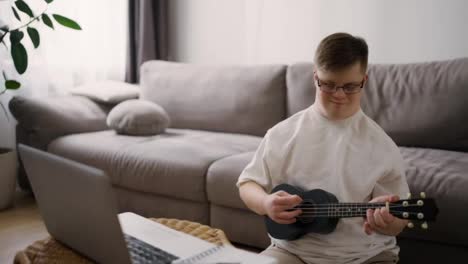 Down-syndrome-guy-having-fun-while-playing-ukulele,-learning-how-to-play-with-laptop