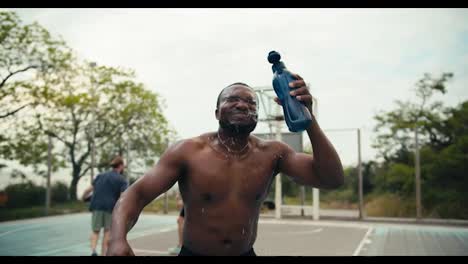 A-man-with-Black-skin-after-playing-basketball-pours-water-on-his-head-from-a-special-bottle-to-cool-off-and-shouts-his-battle-cry-on-the-basketball-court