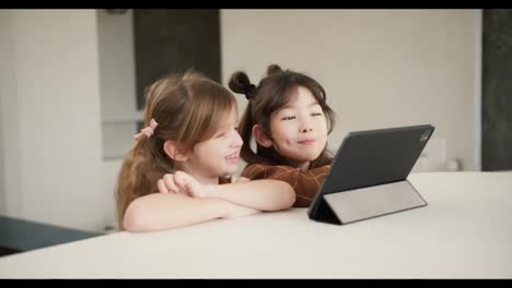 Two-diverse-sisters-using-the-tablet-digital-computer-for-e-learning-or-watching-cartoons