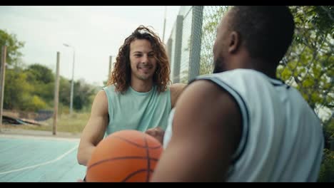 A-curly-red-haired-man-in-a-light-t-shirt-and-a-man-with-Black-skin-in-a-white-t-shirt-are-talking-about-basketball-on-the-basketball-court