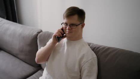 Handsome-Downs-Syndrome-guy-sitting-on-sofa-using-mobile-phone-at-home