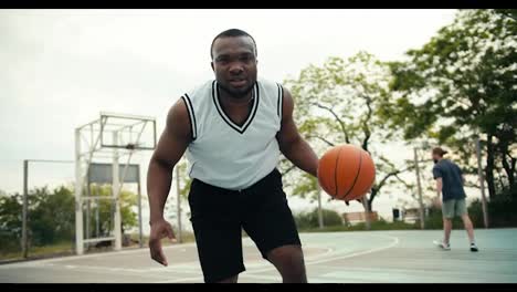 Ein-Junger-Schwarzer-Mann-Im-Weißen-T-Shirt-Zeigt-Im-Sommer-Draußen-Auf-Einem-Basketballplatz,-Wie-Er-Einen-Basketball-Gekonnt-Handhabt