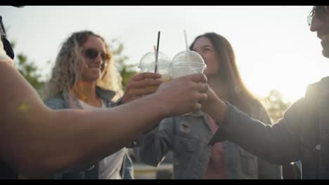 Eine-Gruppe-Junger-Leute-In-Trendigen-Jeansjacken-Klirrt-An-Einem-Sonnigen-Tag-Auf-Der-Straße-Mit-Ihren-Plastikgläsern-Und-Einem-Gelben-Cocktail