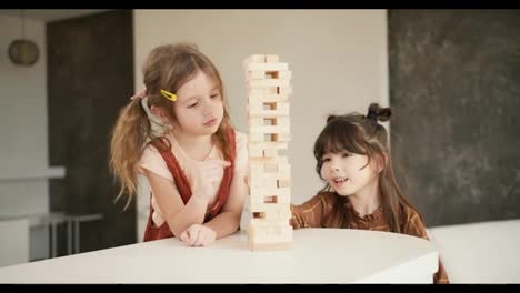 Two-preteen-girls-friends-children-playing-board-game-Jenga-on-table-in-kitchen-at-home