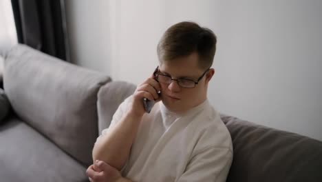 Young-Downs-Syndrome-guy-sitting-on-sofa-using-mobile-phone-at-home