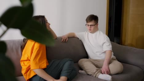 Junge-Paare-Oder-Geschwister-Mit-Down-Syndrom-Unterhalten-Sich,-Während-Sie-Auf-Dem-Sofa-Sitzen
