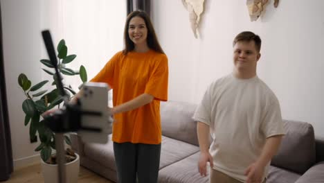 Young-Downs-Syndrome-guy-dancing-in-front-mobile-camera-at-home-with-a-smiling-girl-in-pair