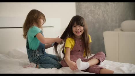 Lovely-little-cute-girl-combing-the-hair-of-her-older-sister-and-while-sitting-on-the-bed-at-home