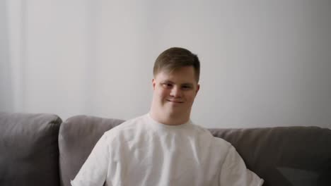 Portrait-of-happy-caucasian-man-with-Down-Syndrome-sitting-on-couch-at-home
