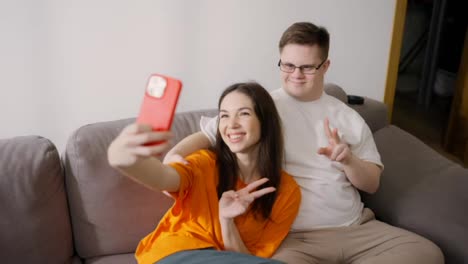 Down-Syndrome-man-sitting-on-sofa-with-a-girl,-they-make-selfie-together