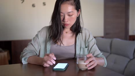 Asiatische-Frau-Mit-Latte,-Die-Den-Bildschirm-Auf-Dem-Smartphone-Berührt