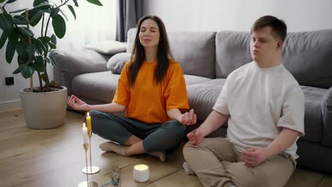 Portrait-of-a-woman-assisting-guy-with-down-syndrome-doing-in-meditating-at-home,-slow-motion