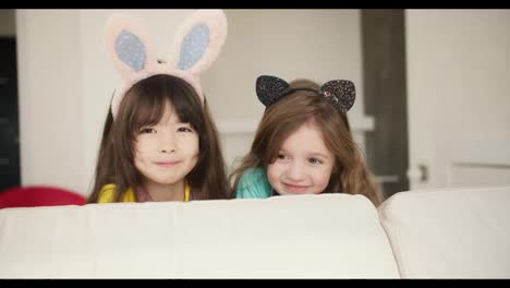 Caucasian-and-asian-looking-female-preschoolers-smiling-to-the-camera,-wearing-funny-bunny-ears