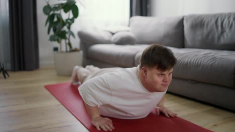 Focused-disabled-man-with-Down-syndrome-doing-push-ups-on-mat-in-living-room