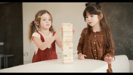 Two-preteen-girls-friends-children-playing-board-game-Jenga-on-table-in-kitchen-at-home,-slow-motion