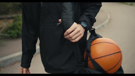 Nahaufnahme-Eines-Mannes-In-Schwarzer-Kleidung,-Der-Einen-Basketball-In-Der-Hand-Hält-Und-Die-Straße-Entlang-Geht