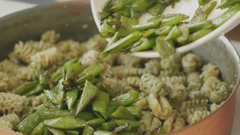 Cook-adding-green-beans-to-pasta-in-pan