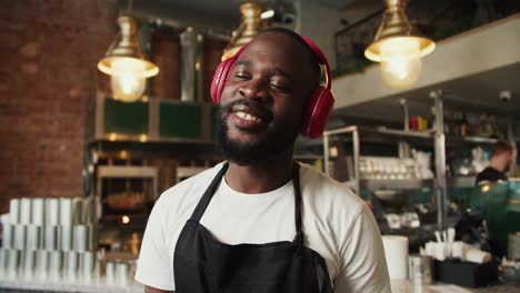 Shooting-close-up:-a-Black-person,-a-guy-in-red-wireless-headphones-in-a-black-apron-is-dancing-in-a-doner-market.-High-quality-video