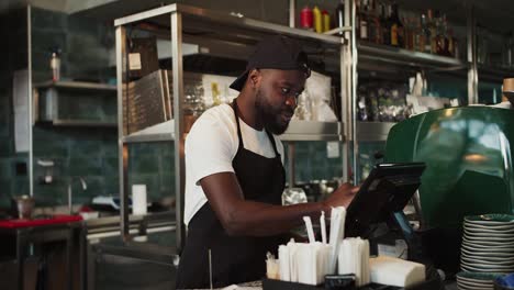 Stilvolle-Schwarze-Person-Mit-Mütze-–-Ein-Mitarbeiter-Des-Dönermarktes-Nimmt-Eine-Bestellung-Entgegen-Und-Arbeitet-An-Einem-Elektronischen-Mann-In-Einem-Café