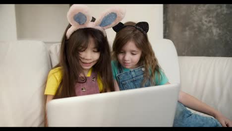 Two-diverse-sisters-using-laptop-for-e-learning-or-watching-cartoons,-wearing-funny-bunny-bands