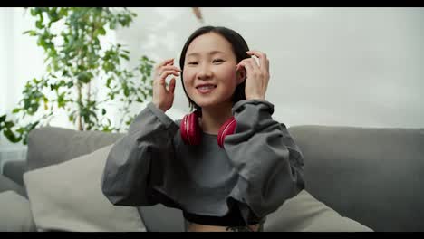 Retrato-De-Una-Amable-Dama-Asiática-Con-Auriculares-Inalámbricos,-Sentada-En-El-Sofá-Y-Sonriendo