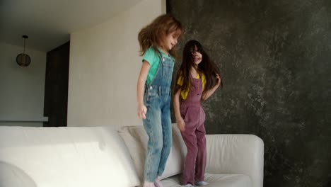 Zwei-Kleine-Schwestern-Haben-Spaß-Daran,-Auf-Das-Weiße-Sofa-Zu-Springen