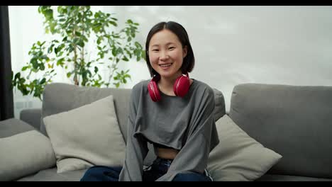 Porträt-Einer-Sanften-Asiatischen-Dame-Mit-Kabellosen-Kopfhörern,-Die-Auf-Der-Couch-Sitzt