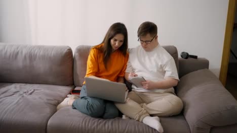 A-guy-with-down-syndrome-writing-notes-from-laptop-at-home-together-with-teacher-or-sister
