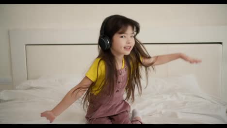 Lovely-asian-looking-listening-to-music-on-smartphone-with-headphones-on-the-bed-and-funny-dancing