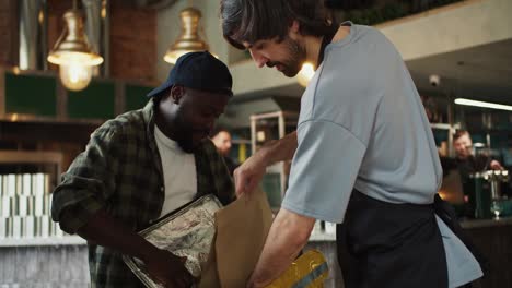 A-market-donor-worker-helps-a-food-delivery-man-place-an-order,-after-which-they-high-five-in-approval.-Teamwork-of-the-restaurant-and-food-delivery